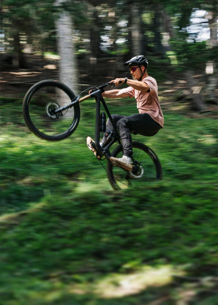 Mountainbiker macht mit seinem Rokua Bike einen Wheelie auf einem Waldweg.