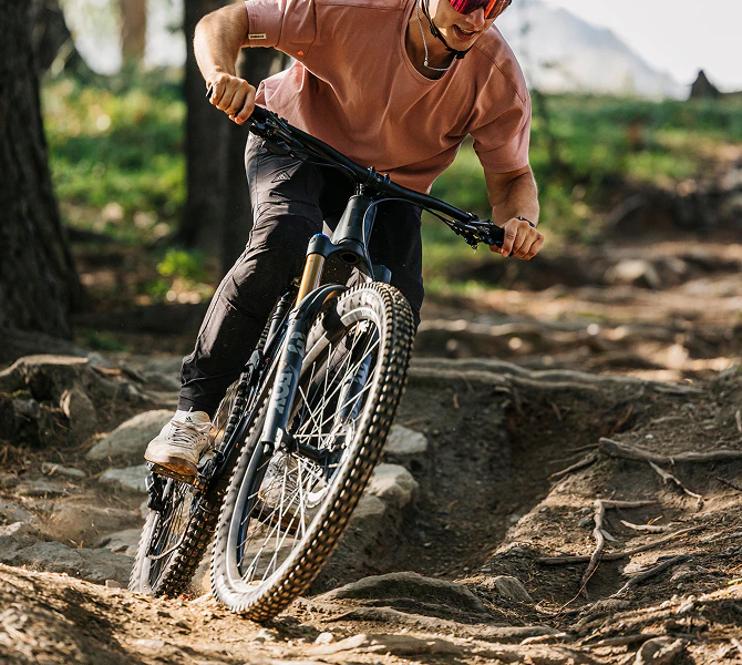 Ein Mountainbiker fährt mit einem schwarzen Rokua Bike über einen wurzeligen Waldpfad.