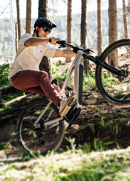 Ein Mountainbiker macht einen Wheelie auf einem Raymon E-Bike mit Avinox-Antrieb im Wald.