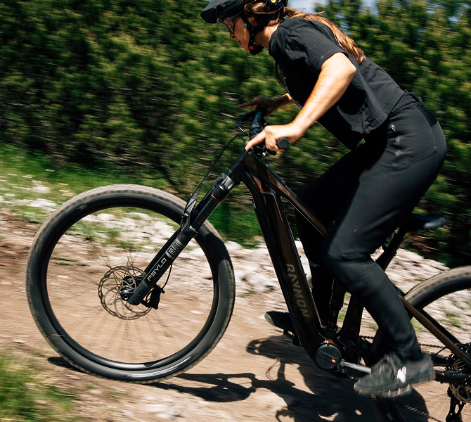 Frau fährt schnell mit einem Raymon Durok E-Mountainbike einen steilen Waldweg hoch.