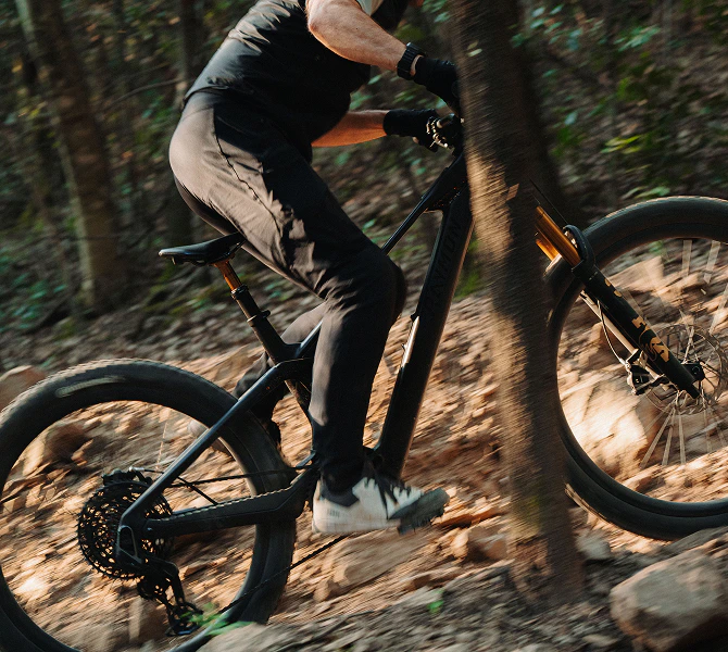 Ein Fahrer steuert sein schwarzes Raymon Tarok E-Mountainbike rasant über einen steinigen Waldtrail.