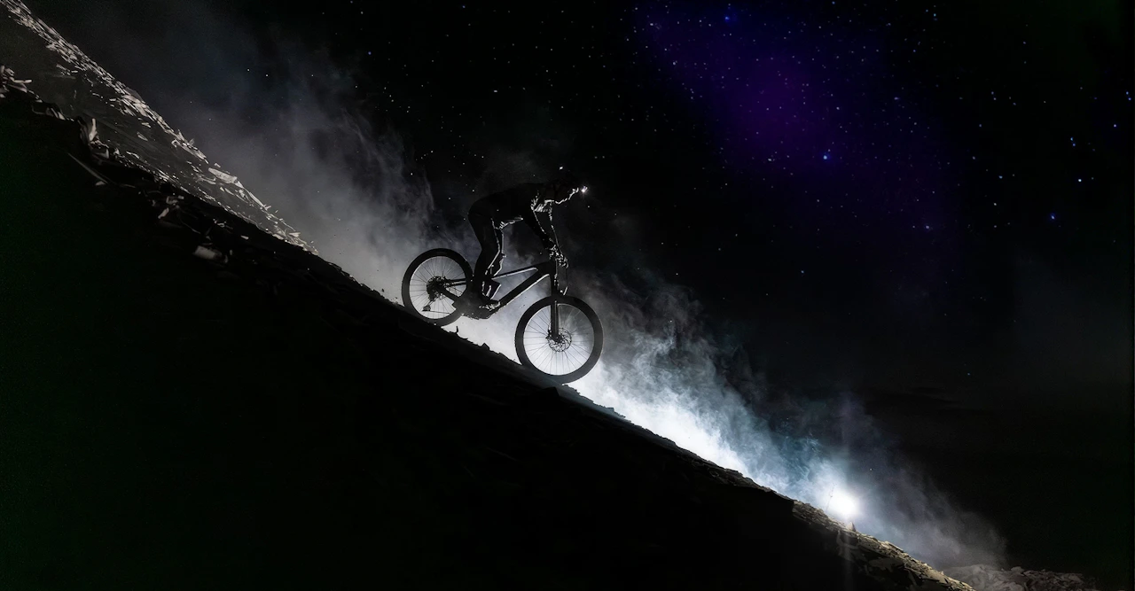 Ein Mountainbiker fährt bei Nacht auf einem Raymon Tarok mit DJI Avinox System einen steilen, nebligen Hang hinunter.