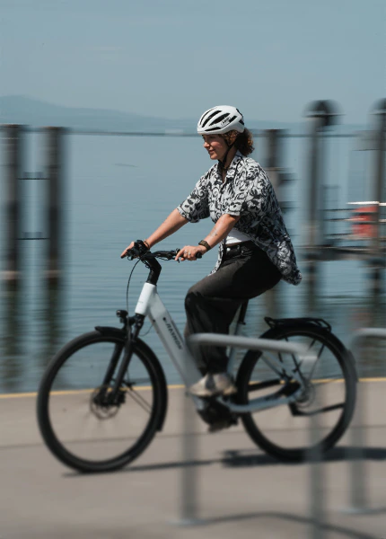 Frau fährt mit einem weißen Raymon Numa E-Bike an einer Uferpromenade.