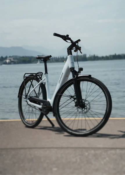 Weißes Numa E-Bike von Raymon steht auf einer Promenade vor einem See.