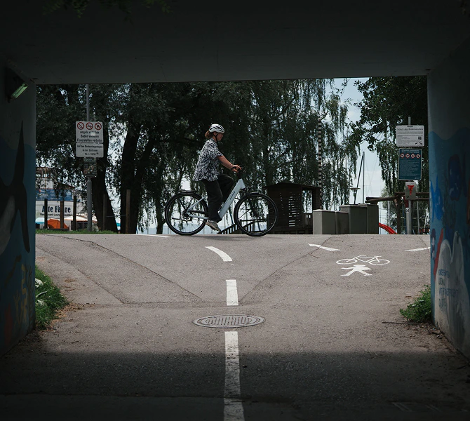Eine Person fährt auf einem hellen Numa E-Bike an einer Wegkreuzung vorbei.