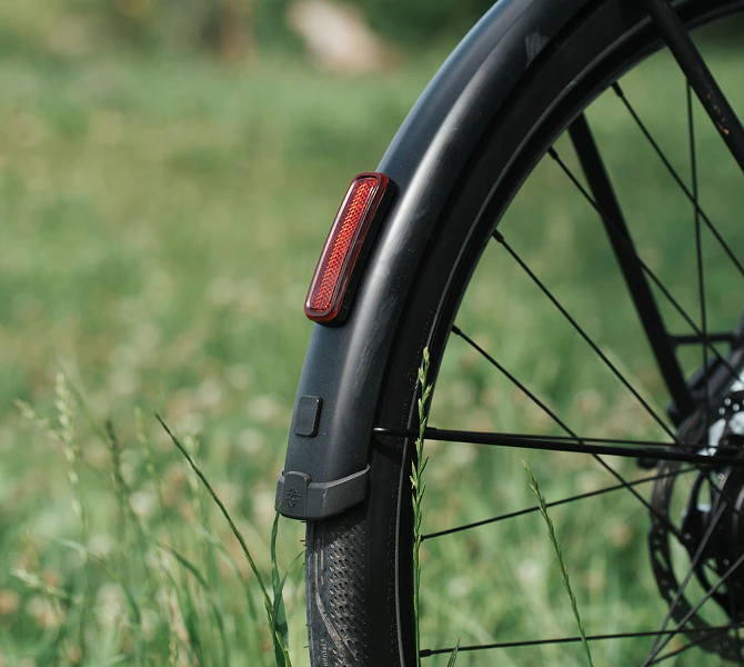 Roter Reflektor an einem schwarzen Schutzblech eines Numa E-Bikes vor grüner Wiese.