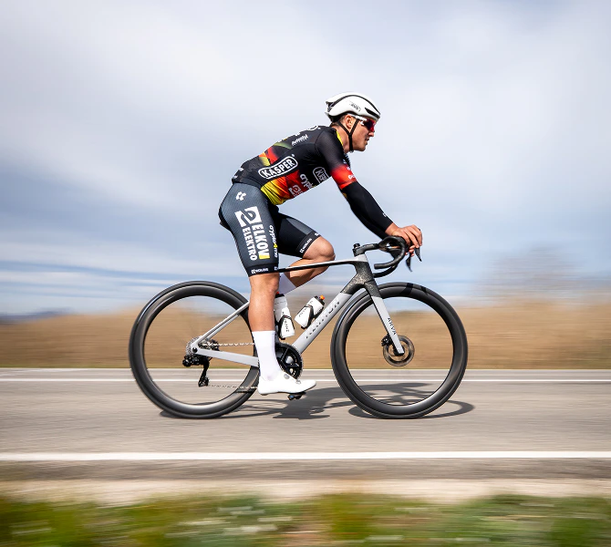 Radsportler im Elkov-Kasper-Trikot fährt ein graues Arva Rennrad auf einer Asphaltstraße.