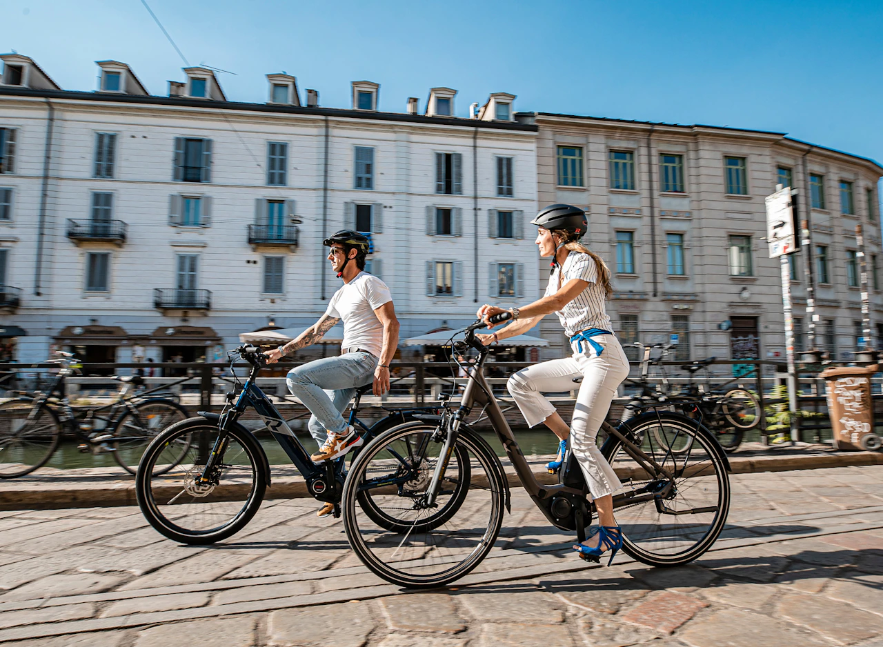 Ein Paar fährt auf Raymon E-Bikes durch eine sonnige Stadt.