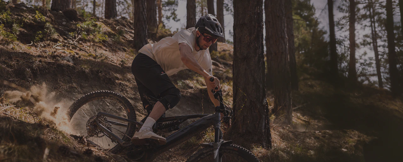 Mountainbiker mit Helm fährt rasant auf einem Raymon E-MTB durch einen Nadelwald.