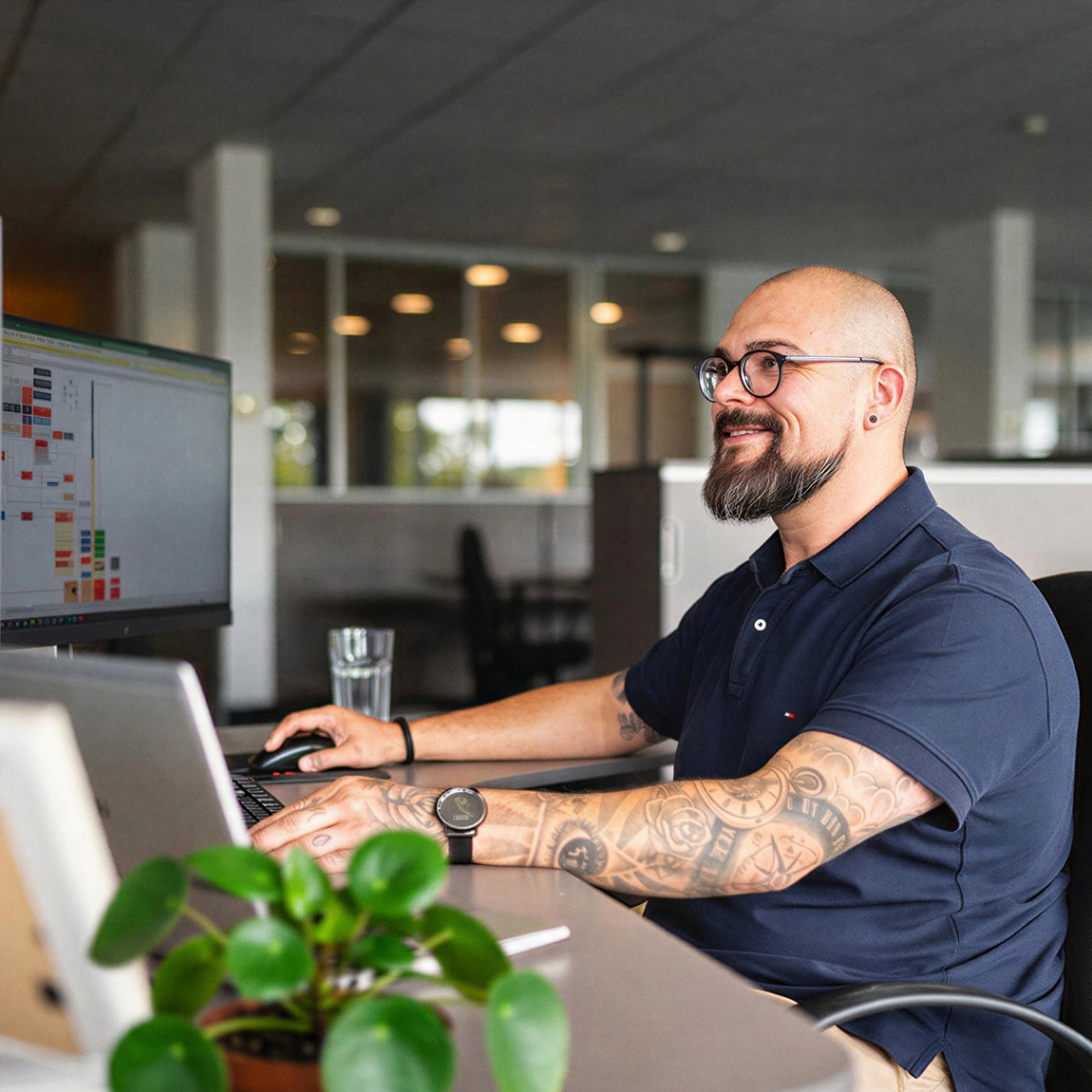 Ein lächelnder Mitarbeiter von Raymon arbeitet an seinem Bildschirmarbeitsplatz im Büro.