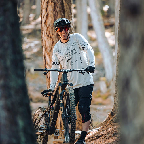 Mountainbiker Johannes Fischbach lächelt beim Schieben seines E-Bikes durch den Nadelwald.
