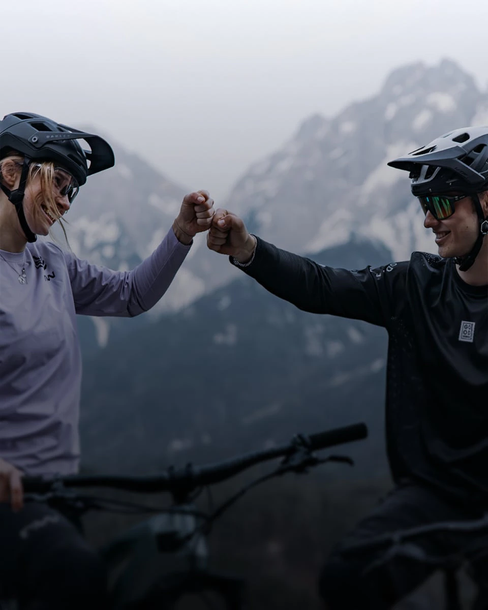 Zwei Mountainbiker geben sich vor einer Bergkulisse einen Fistbump.