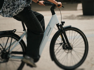 Junge Frau mit sportlichen Schuhen und schwarzer Hose fährt auf einem weißen Numa E-Bike durch die Stadt.